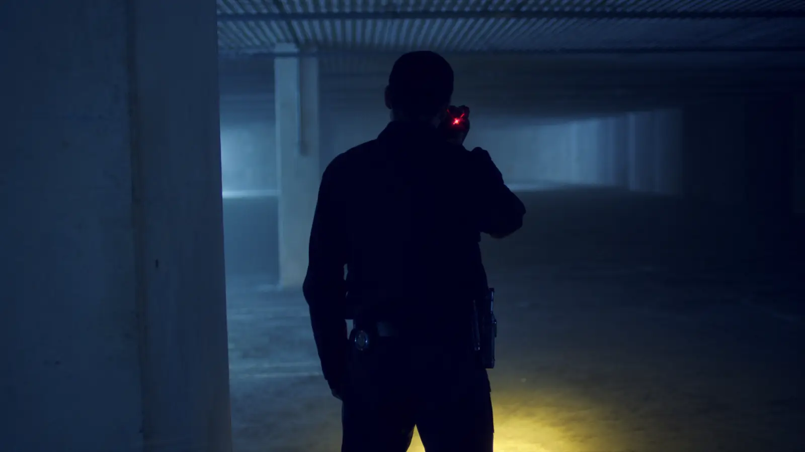 A guard seen from behind in a covered parking garage, with his flashlight