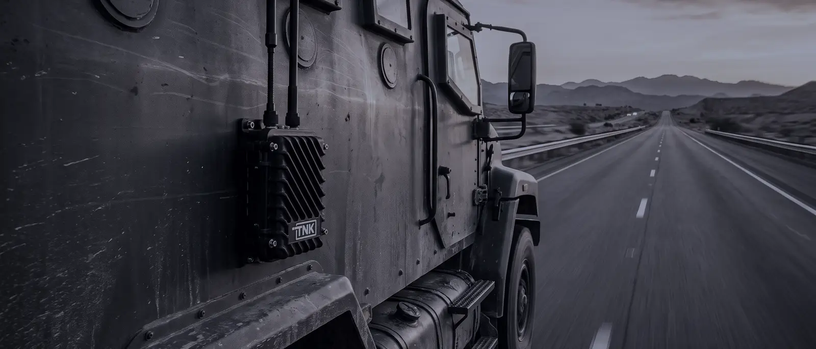 Tank unit mounted on the side of an armored truck driving down a highway at sunset